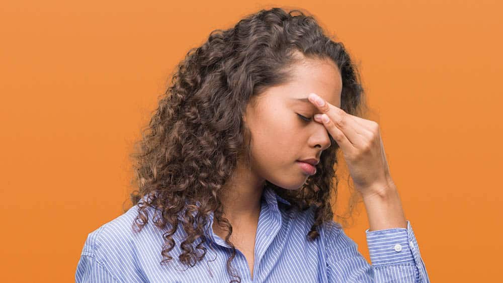 Mulher pressionando com a mão a região entre os olhos, local típico de dor em caso de sinusite.