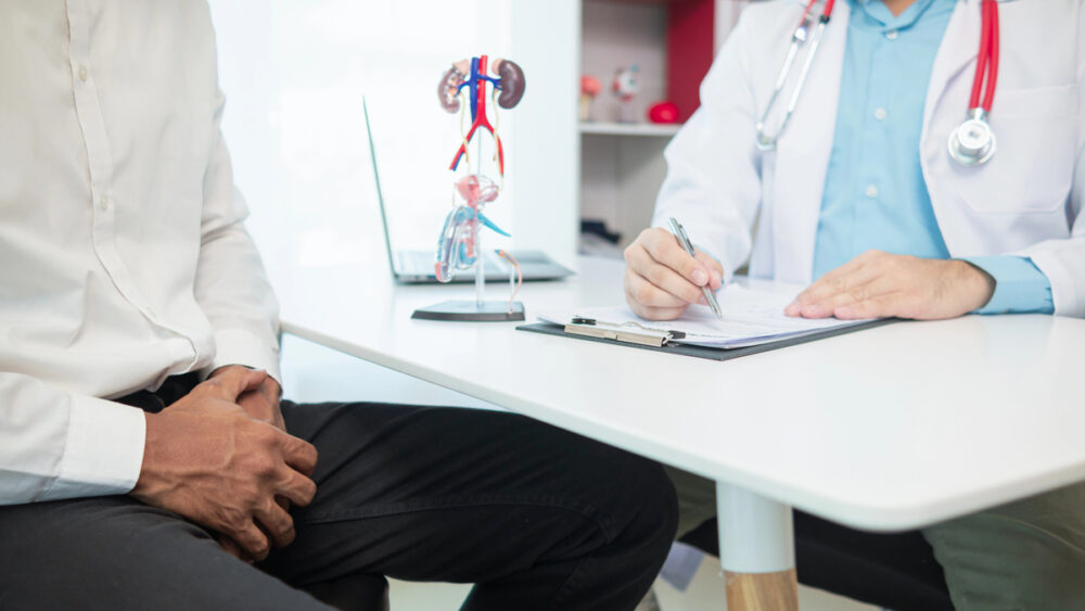 paciente em consultório, com a mão no pênis, conversa com médico