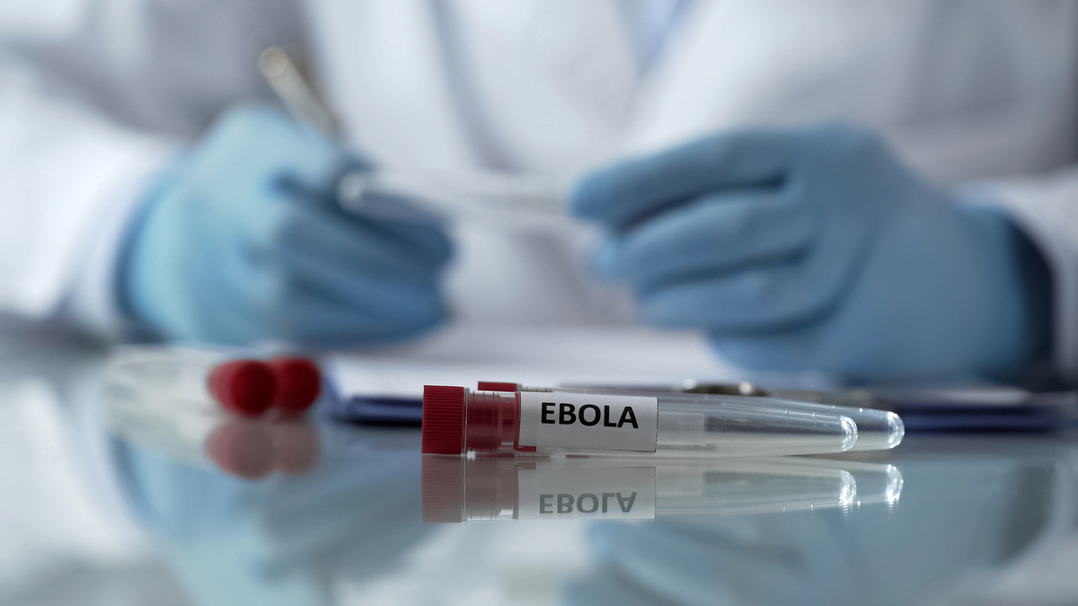 close em vidro de exame para Ebola à frente de mão de médico com luvas