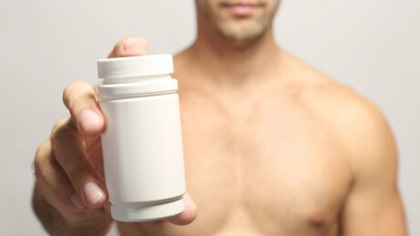 homem musculoso mostra vidro de medicamento. uso de testosterona para ganho de massa muscular traz riscos