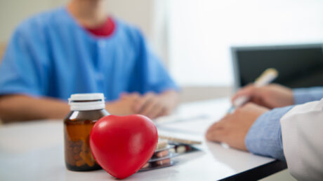 médico atende paciente. sobre a mesa, frasco de medicamento e coração de borracha. cardiomegalia, conhecida como "coração grande", pode trazer problemas