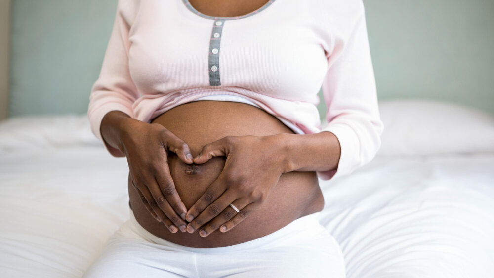 close em barriga de mulher grávida sentada n cama. Transmissão vertical do HIV pode ser impedida.