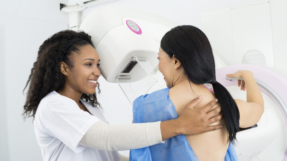 técnica ajuda paciente a se posicionar para realizar a mamografia