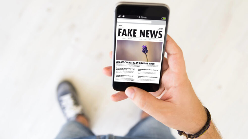 close em mão de jovem segurando o celular onde se lê "fake news"