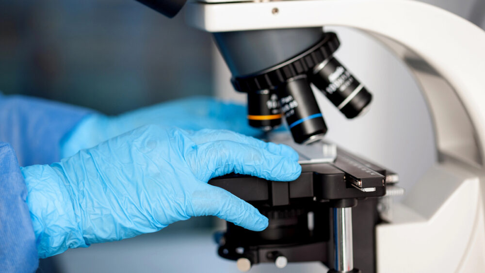 mão de pesquisador com luva colocando lâmina no microscópio