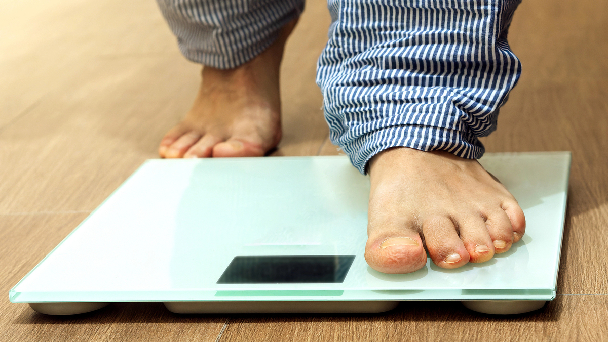 close de pernas de homem com obesidade subindo na balança