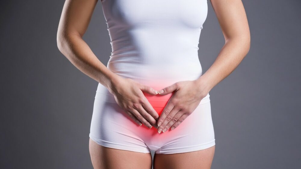 Woman in white underwear presses her lower abdomen, with a red glow at the pelvic area indicating pain or discomfort.