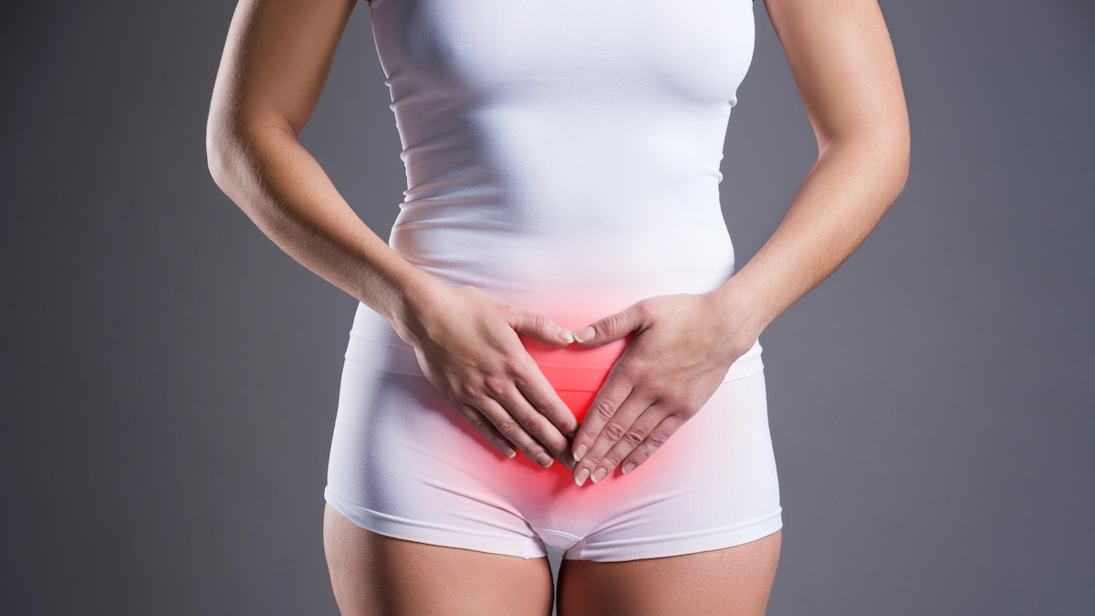 Woman in white underwear presses her lower abdomen, with a red glow at the pelvic area indicating pain or discomfort.