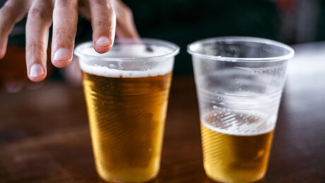 close em copos de cerveja sobre balcão sendo alcançados por dedos masculinos