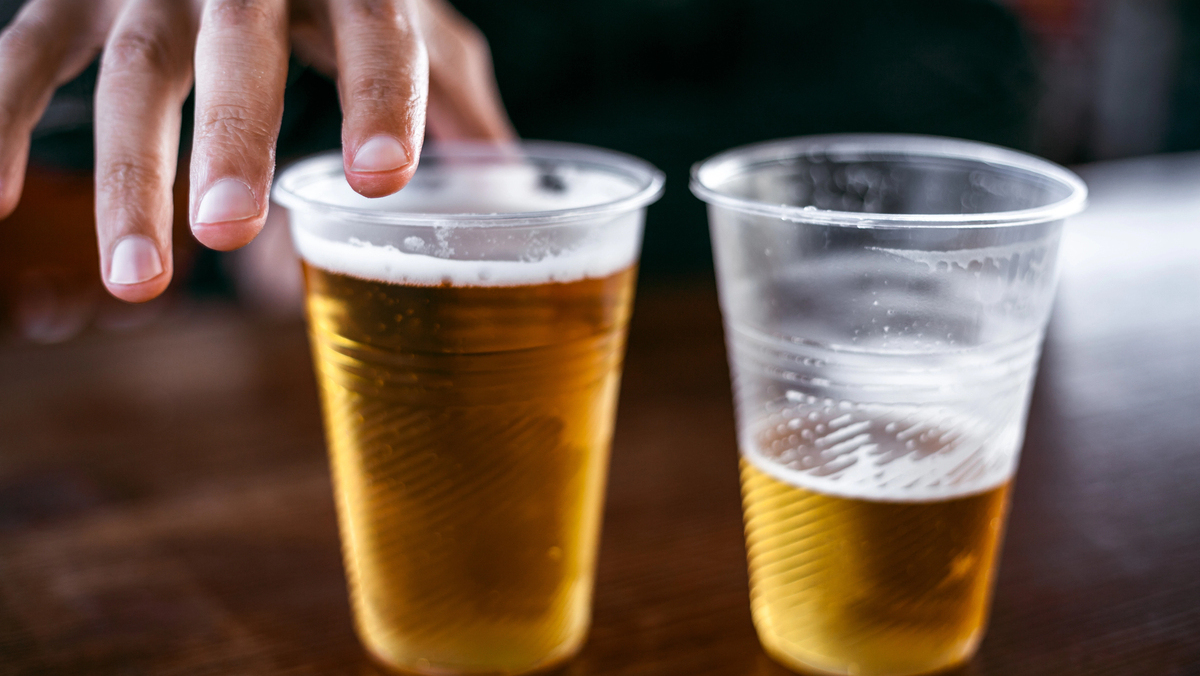 close em copos de cerveja sobre balcão sendo alcançados por dedos masculinos