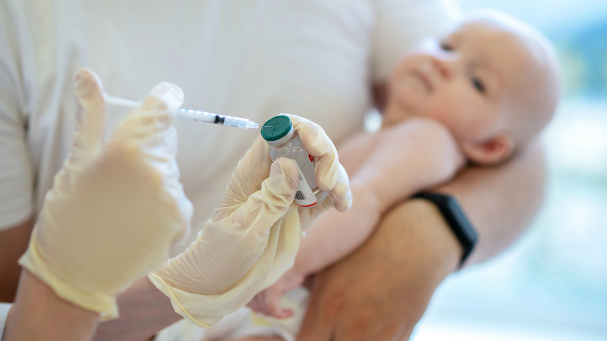 mão de médica com seringa e frasco de vacina e bebê no colo prestes a receber vacina contra o sarampo