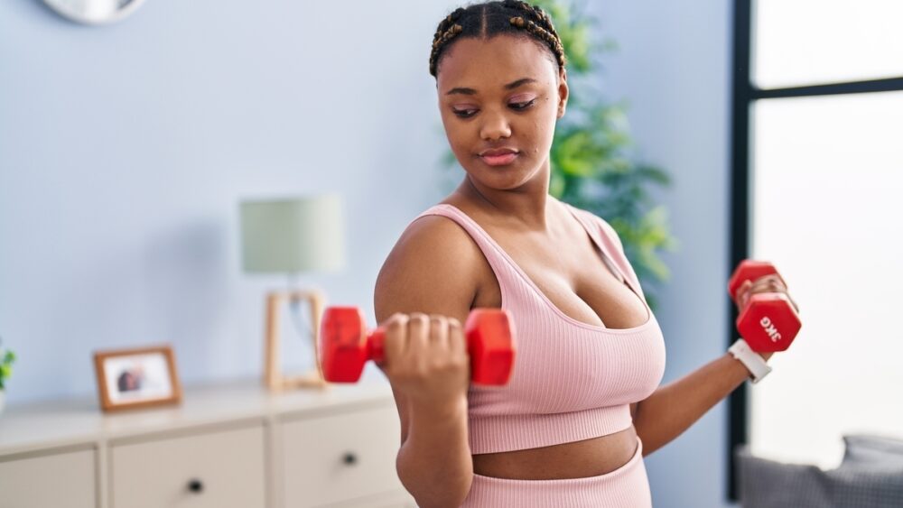 mulher faz musculação com pesos na sala de casa