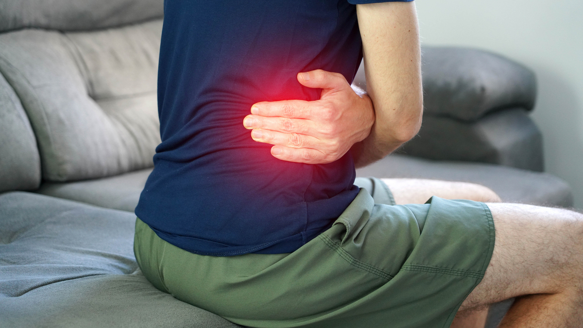 homem sentado, com mão nas costas, em sinal de cólica renal